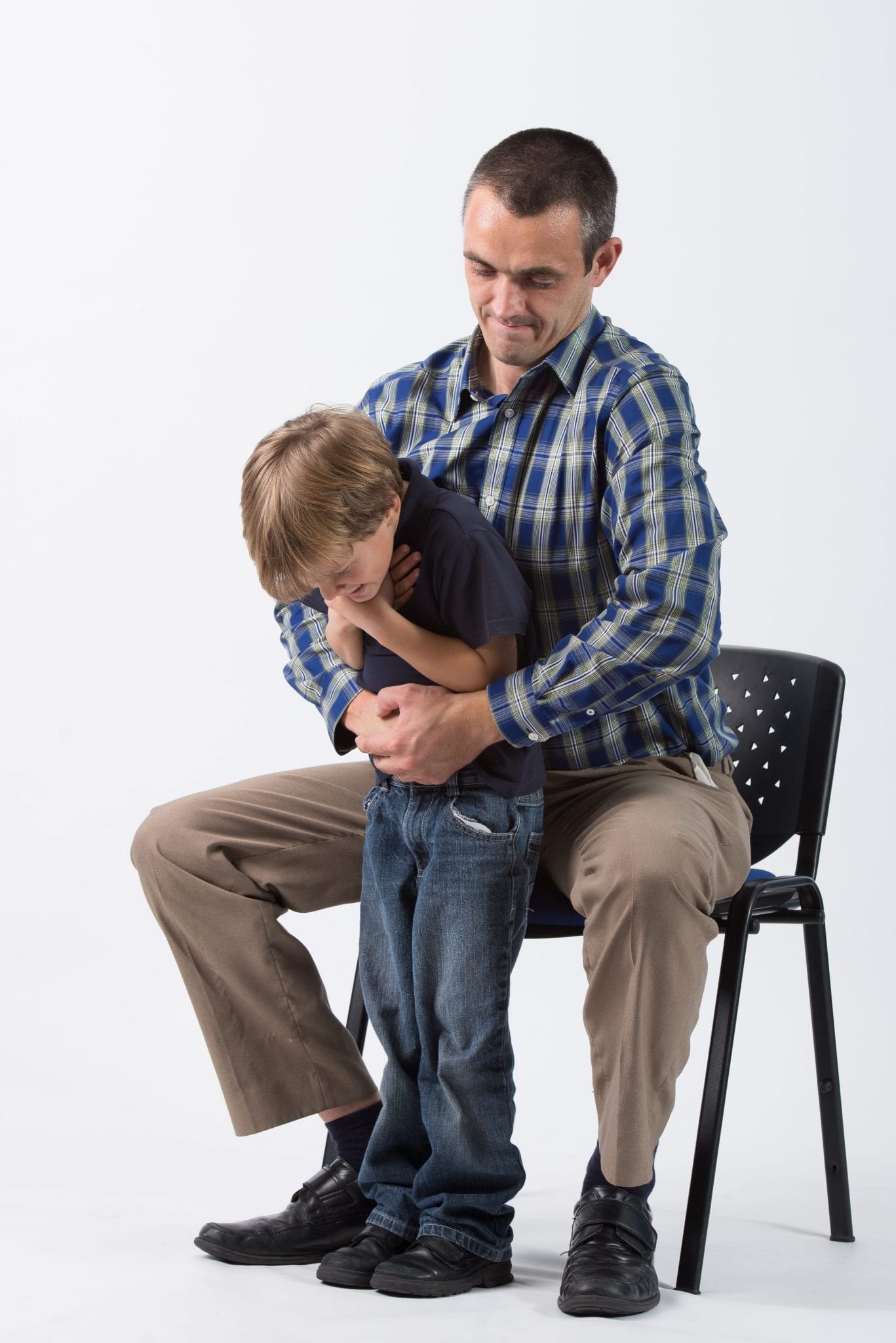 A man sat down preforming the Heimlich maneuver on a small boy.