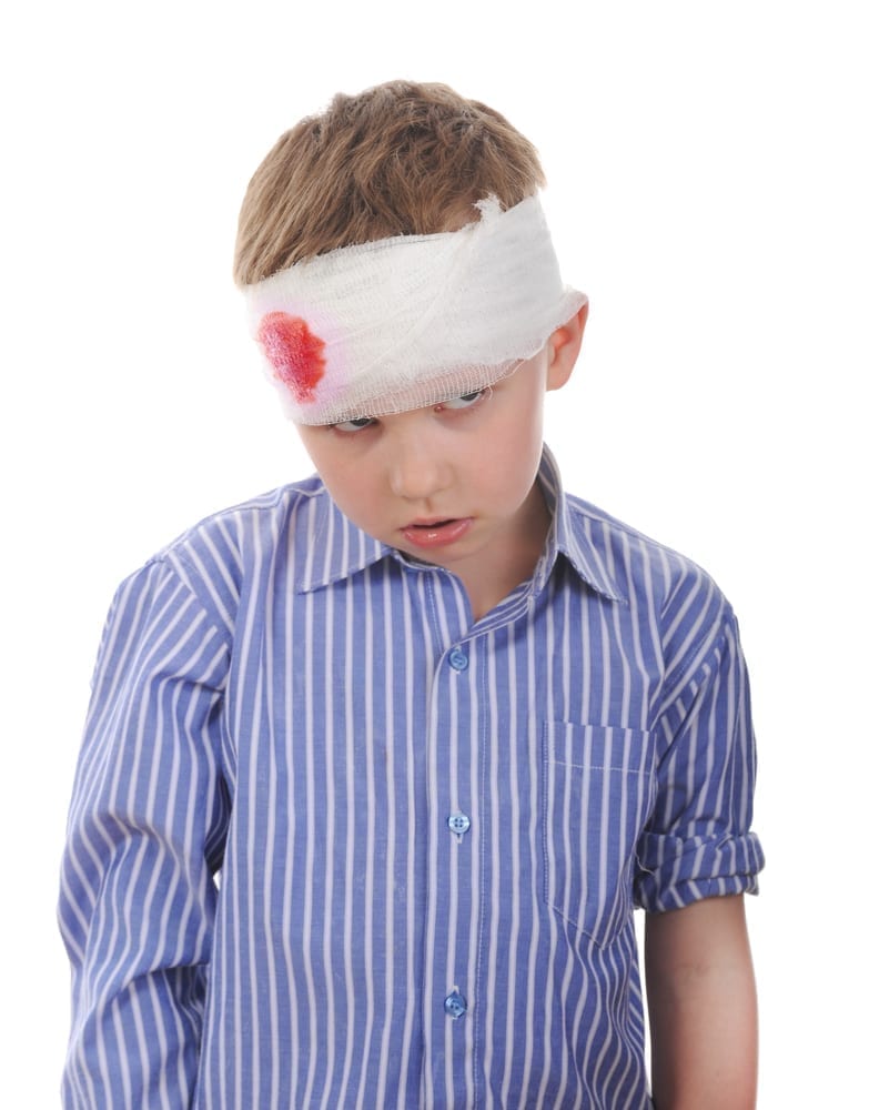 A young booy with a bandage on his head with blood seeping through.